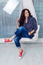 Swag style. Hipster girl smiling at the camera and sitting on a swing. Young caucasian girl with dark curly hair wearing a blue Royalty Free Stock Photo