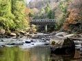 Swallow Falls State Park in Maryland with the water in the foreground, large rocks, and fall foliage trees and a bridge in the Royalty Free Stock Photo