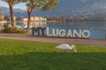 Swan on a meadow in front of metal inscription with the name of city of Lugano