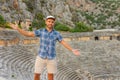 Swarthy caucasian european guy in a plaid shirt in a cap with his arms outstretched smiles at the ancient unique famous places in