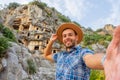 Swarthy caucasian european guy in plaid shirt smiles rejoices makes a selfie in a brown hat at the ancient unique landmarks Turkey