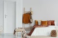 Sweaters, wicker hat and bag on wooden ladder next to king size bed with velvet pillows in white bedroom interior, copy space on Royalty Free Stock Photo