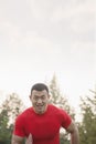 Sweating, tired, muscular man with a red shirt running toward camera in a park in Beijing, China