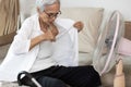 Sweaty asian senior woman opening shirt,cooling herself in front of a fan,stay at home,trying to refresh with electrical fan,tired Royalty Free Stock Photo