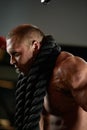 Sweaty man resting after working out with ropes. Photo of sporty man with naked torso on dark background. Strength and