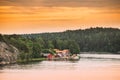 Sweden. Many Beautiful Red Swedish Wooden Log Cabins Houses On Rocky Island Coast In Summer Evening. Lake Or River