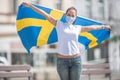 Swedish girl on a street holds flag in her hands celebrating, wearing a face mask Royalty Free Stock Photo