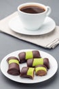 Swedish sweets punsch rolls or punschrullar, covered with green marzipan, on white plate, served with coffee, vertical