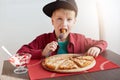 Sweet adorable child, boy in stylish cap and red shirt eating pizza and ice-cream at a restaurant. Fashion little boy having break Royalty Free Stock Photo