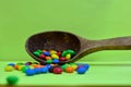 Sweet assorted multicolored chocolates, gum balls in a wooden spoon on a green photon or tablets and vitamins. Royalty Free Stock Photo