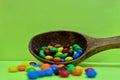 Sweet assorted multicolored chocolates, gum balls in a wooden spoon on a green photon or tablets and vitamins. Royalty Free Stock Photo