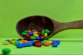 Sweet assorted multicolored chocolates, gum balls in a wooden spoon on a green photon or tablets and vitamins. Royalty Free Stock Photo