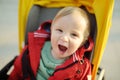 Sweet baby boy wearing red jacket sitting in a stroller outdoors. Little child in pram. Infant kid in pushchair. Spring walks with Royalty Free Stock Photo