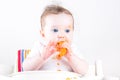 Sweet baby eating a carrot in a white high chair Royalty Free Stock Photo