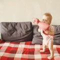 Sweet baby girl standing on her little feet on a couch at home, playing Royalty Free Stock Photo