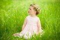 Sweet baby girl in wreath of flowers sitting on green grass Royalty Free Stock Photo