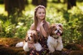 Sweet beautiful girl hugs two identical Shih Tzu dogs on a clearing in the forest