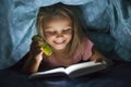 Sweet beautiful and pretty little blond girl 6 to 8 years old under bed covers reading book in the dark at night with torch light Royalty Free Stock Photo