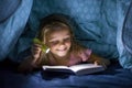 Sweet beautiful and pretty little blond girl 6 to 8 years old under bed covers reading book in the dark at night with torch light Royalty Free Stock Photo