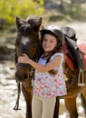 Sweet beautiful young girl 7 or 8 years old hugging head of little pony horse smiling happy wearing safety jockey helmet in summer Royalty Free Stock Photo