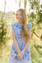 A sweet and beautiful young smiling woman in a blue dress with flowers and long blonde hair. Summer portrait of a happy girl Royalty Free Stock Photo