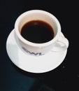 sweet black coffee in a white cup and a white plate on a black table Royalty Free Stock Photo