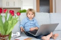 Sweet blond child, boy in casual clothes, woring on computed at home