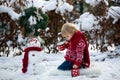 Sweet blond toddler child, boy, playing in garden with snow, making snowman, happy kid winter time Royalty Free Stock Photo