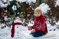 Sweet blond toddler child, boy, playing in garden with snow, making snowman, happy kid winter time Royalty Free Stock Photo