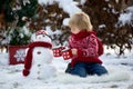 Sweet blond toddler child, boy, playing in garden with snow, making snowman, happy kid winter time Royalty Free Stock Photo