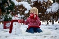 Sweet blond toddler child, boy, playing in garden with snow, making snowman, happy kid winter time Royalty Free Stock Photo