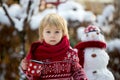 Sweet blond toddler child, boy, playing in garden with snow, making snowman, happy kid winter time Royalty Free Stock Photo