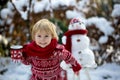 Sweet blond toddler child, boy, playing in garden with snow, making snowman, happy kid winter time Royalty Free Stock Photo