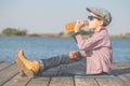 Sweet boy boy sitting by the river and drinking juice Royalty Free Stock Photo