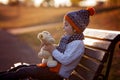 Sweet boy, sitting on bench with teddy bear on sunset