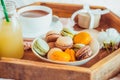 Sweet breakfast in bed for lover. Close up macaroons, cup of coffee, juice, flower and gift box on wooden tray. Romantic breakfast Royalty Free Stock Photo