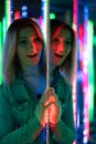 Sweet caucasian girl walks in a mirror maze with colorful diodes and enjoys an unusual attraction room in the city