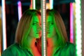 Sweet caucasian girl walks in a mirror maze with colorful diodes and enjoys an unusual attraction room in the city