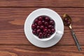 Sweet cherries in a white cup and a teaspoon on a wooden table, selected focus, top view Royalty Free Stock Photo