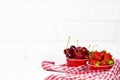 Sweet Cherry and Juicy Fresh Strawberries in a Red Bowl on a piece of cloth on a white Brick background. Vitamin food