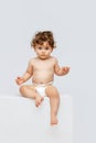 Vertical portrait of little cute toddler boy, baby in diaper sitting, pouting lips isolated over white studio background Royalty Free Stock Photo