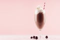 Sweet chocolate milkshake in exquisite wineglass decorated candy balls, whipped cream, straw on light pastel pink background.