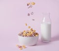 Sweet colorful cornflakes rings fly in a white bowl with a bottle of milk on a pink background. Front view and copy space