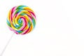 Sweet colorful spiral shaped lollipop lying in upper left corner, isolated on white background, top view. Royalty Free Stock Photo