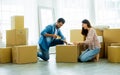 Sweet couple moving to new house or apartment, smiling with happiness, helping each other to open cotton boxes while sitting on Royalty Free Stock Photo