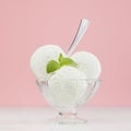 Sweet creamy ice cream in elegant transparent glass bowl with green mint, silver spoon on white wood table and pastel pink wall. Royalty Free Stock Photo