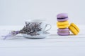 Delicious violet and yellow macarons and cup of latte or americano and branch of fragrant lavender on white wooden