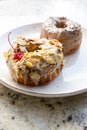 A plate with two tasty glazed donuts with chocolate, nuts and red cherry