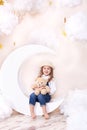 Sweet Dreams. Little cute girl sitting on the moon with clouds and stars with a teddy bear in their hands and playing. Little astr