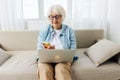 sweet elderly lady sitting on the sofa in her apartment and attentively looking at her smartphone holding it in her hand